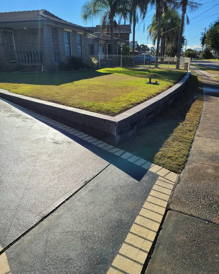 Charcoal block retaining wall holding a raised front lawn beside a driveway