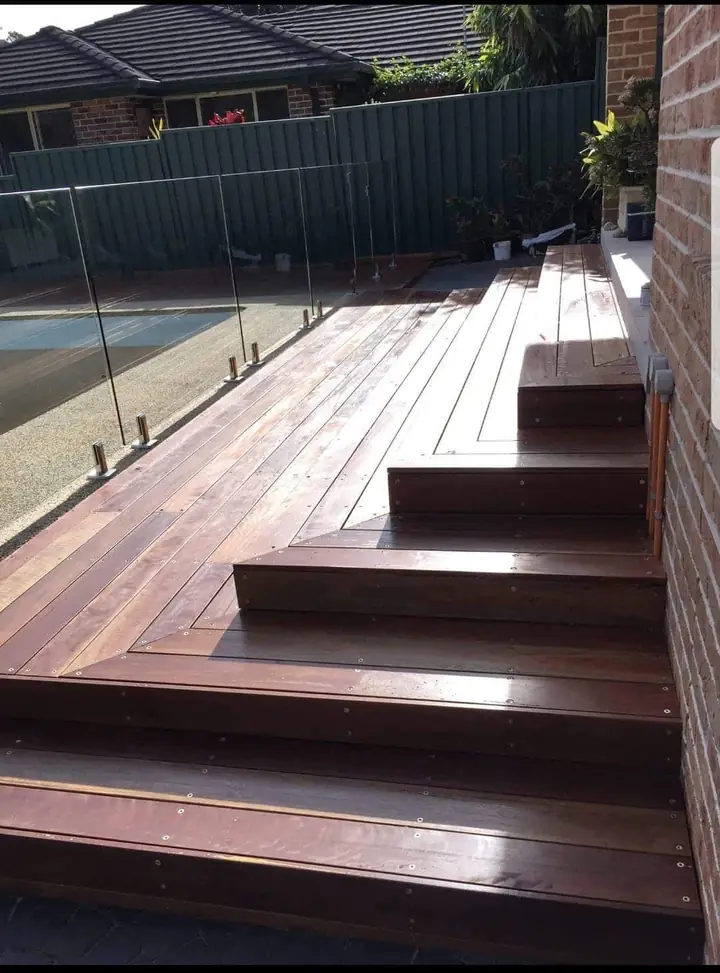 Merbau deck with wide steps running along a pool with glass fencing