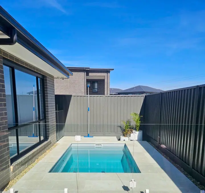 Plunge pool with pale stone paving and frameless glass fencing